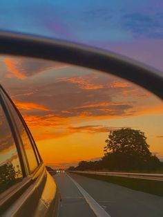 the sun is setting on an empty road as seen through a car's rear view mirror