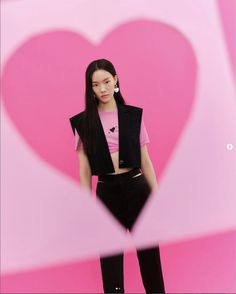 a woman standing in front of a pink background with a heart shaped cut out on it