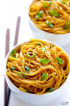 two white bowls filled with noodles and garnished with green onions, chopsticks