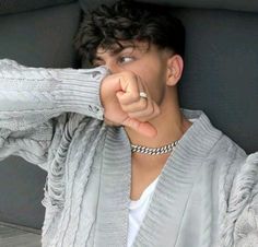 a young man is pointing his finger at the camera while wearing a gray sweater and white t - shirt