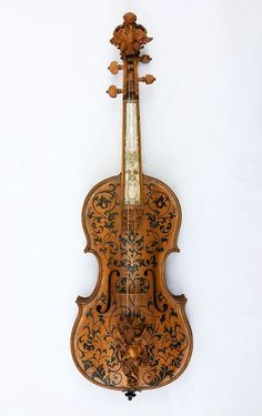 an old violin hanging on the wall in front of a white wall with black and gold designs