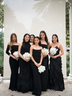 a group of women standing next to each other wearing black dresses and holding bouquets