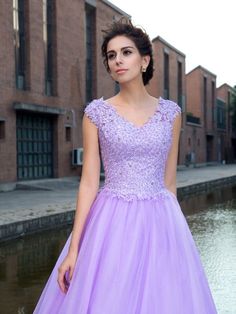 a woman in a purple dress standing next to a body of water with brick buildings behind her