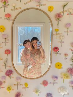 a woman taking a selfie in front of a mirror with flowers on the wall