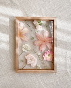 a wooden frame with pink flowers in it on a white cloth covered tablecloth background