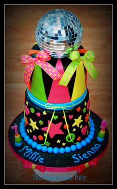 a colorful cake with disco balls and ribbons on it's top, sitting on a wooden table