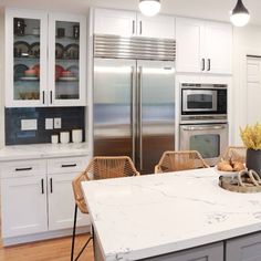 a kitchen with white cabinets and marble counter tops in front of stainless steel refrigerators