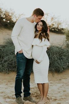 a pregnant couple standing in the sand together