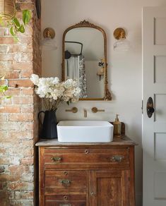 a bathroom sink sitting under a mirror next to a wooden cabinet with flowers in it