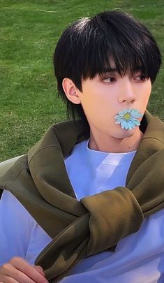 a young man sitting on top of a grass covered field with a flower in his mouth