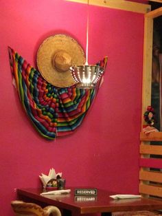 a room with pink walls and wooden tables in front of a large hat hanging on the wall