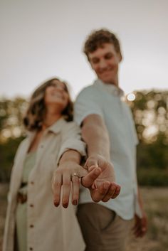 a man and woman holding hands in the middle of an open field with trees in the background