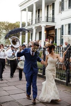 a bride and groom walking down the street holding an umbrella in front of a large group of people