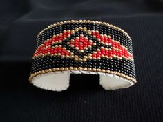 a black, red and gold beaded cuff on a black cloth with white beads