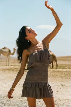 a woman standing in the desert with her arms up and camels in the background