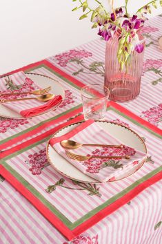 the table is set with pink and green place mats, silverware, and flowers