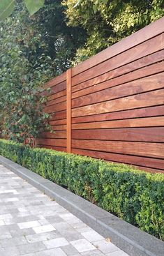 a wooden fence next to a brick walkway and shrubbery on the side of a building