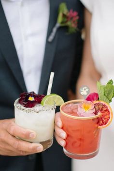 a bride and groom holding up cocktails in their hands with garnishes on them