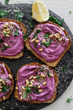 four pieces of bread with purple spread on them and garnished with nuts, parsley and lemon wedges