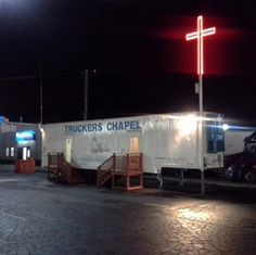 a white truck parked in front of a gas station at night with a cross on it's side