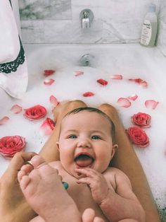 a woman holding a baby in a bathtub with rose petals on the floor next to it