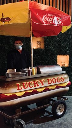 a man wearing a face mask standing behind a hot dog cart