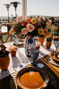 a table set with plates and vases filled with flowers