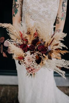 a woman in a white dress holding a bouquet filled with dried flowers and foliages