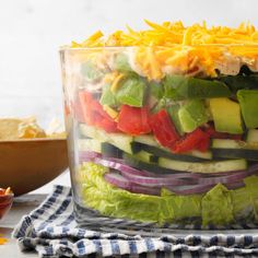 a salad in a glass container with lettuce, tomatoes, cucumber and cheese