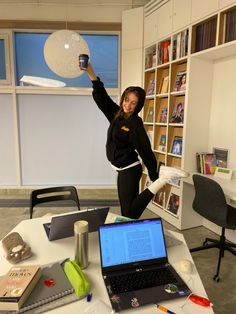 a woman in black jumps up into the air while holding a coffee cup above her head