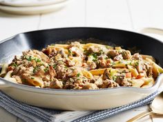 a skillet filled with pasta and meat on top of a white tablecloth next to silverware