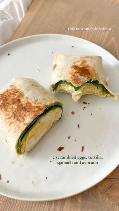 an egg, spinach and avocado burrito cut in half on a white plate