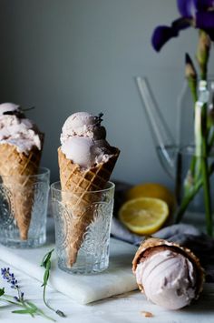 three ice cream cones sitting on top of a table next to some flowers and lemon slices