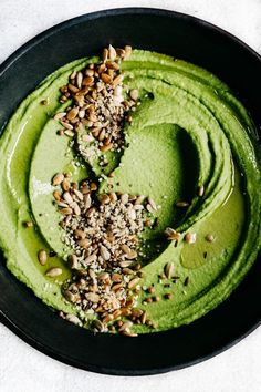 a black bowl filled with green smoothie and nuts on top of it, next to a spoon