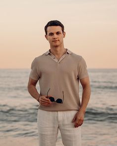 a man standing in front of the ocean with his hands on his hips and looking at the camera