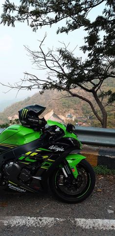 a green and black motorcycle parked on the side of a road next to a tree