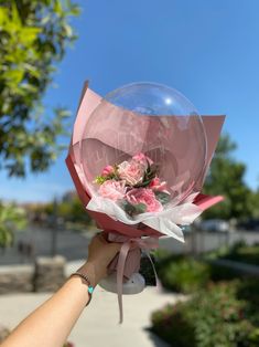 a person holding up a pink flower bouquet in front of a blue sky and some trees