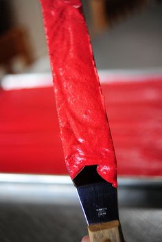 a person holding a knife with red cloth on it's handle and wooden block