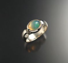 "This is a very bright and colorful natural Opal from Ethiopia. Set in a bezel east-west style with a 6mm wide low dome smooth band. The stone is clean and displays mint green and powder blue colors in a crystal base. Stone measures 8x10mm. Specify your ring size in a \"note to seller\" at check out." Modern Oval Cabochon Opal Ring, Modern Oval Opal Ring With Bezel Setting, Green Domed Jewelry With Polished Finish, Modern Green Round Dome Ring, Modern Opal Ring With Bezel Setting, Green Oval Opal Ring With Bezel Setting, Powder Blue Color, Opal Ring, East West