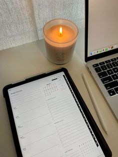 a tablet with a calendar on it next to a laptop computer and a lit candle