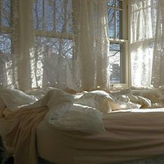 an unmade bed in front of a window with sheer curtains on the windowsill