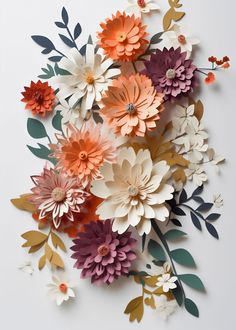 an arrangement of paper flowers on a white surface with green leaves and orange ones in the center