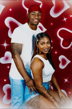 a man and woman are posing for a photo together with hearts on the wall behind them