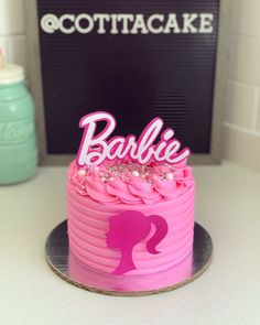 a pink cake sitting on top of a counter next to a sign that says barbie