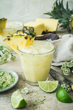 a pineapple margarita is garnished with limes and sliced pineapple on the side