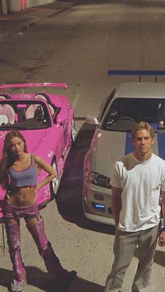 a man and woman standing next to two cars with pink paint on the hoods