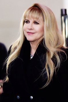 a woman with long blonde hair wearing a black coat