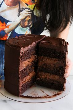 a chocolate cake on a plate with one slice cut out and someone holding the rest of the cake