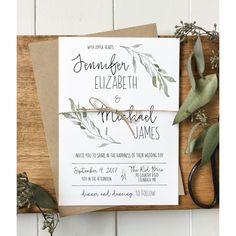 the wedding stationery is laid out on top of a cutting board with scissors and greenery