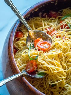 a wooden bowl filled with spaghetti and tomatoes